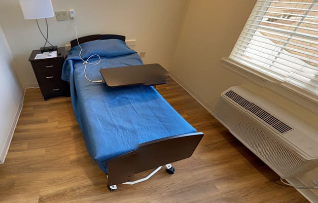 A neatly made bed with a blue blanket and a bedside table.