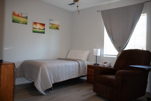 A neatly arranged bedroom with a bed, brown recliner, and artwork on the wall.