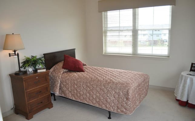 A simple, well-furnished resident room with a bed and lamp.
