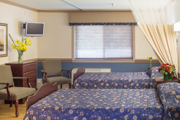 Interior of a shared room with two beds, chairs, and floral decorations.