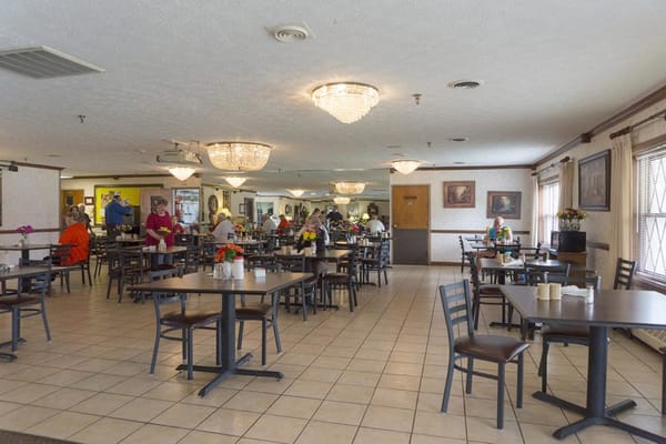 A spacious dining room with tables set for meals and residents enjoying their time.
