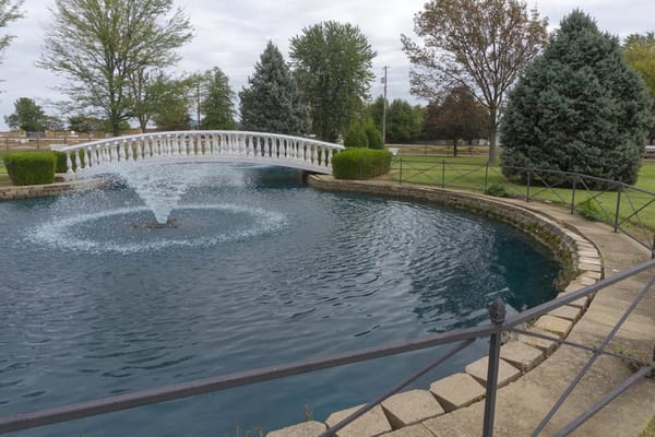 A decorative pond with a fountain and a white bridge at Fern Terrace of Owensboro.