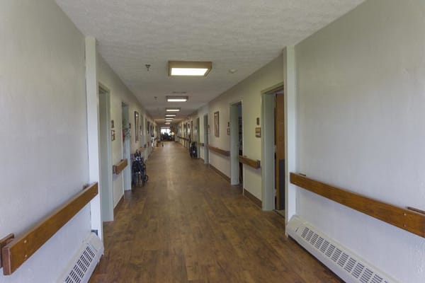 A wide hallway in the senior living facility with wooden floors and doorways on either side.