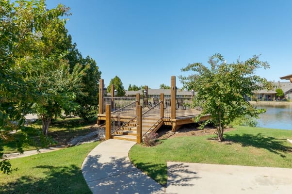 A wooden deck leading to a lake surrounded by greenery.