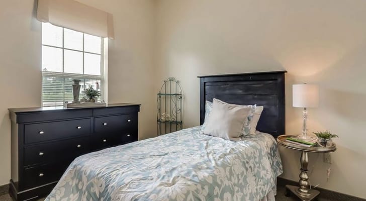 A well-decorated bedroom with a single bed, dresser, and window light.