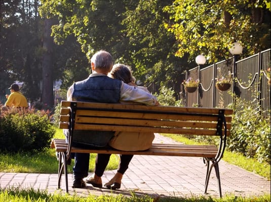 Elderly couple sitting closely on a bench in a garden
