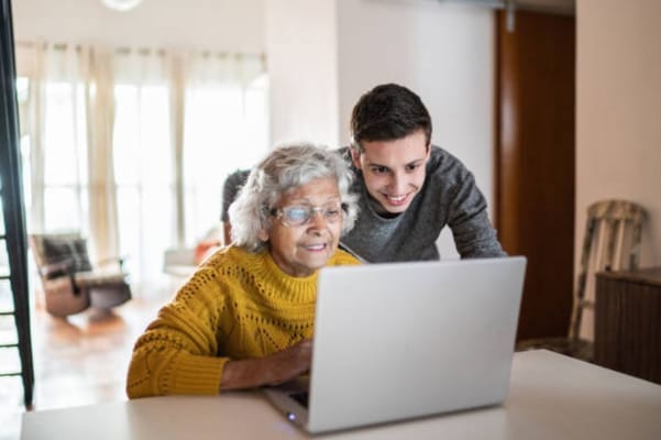 A senior woman and a young man smiling while using a laptop together.
