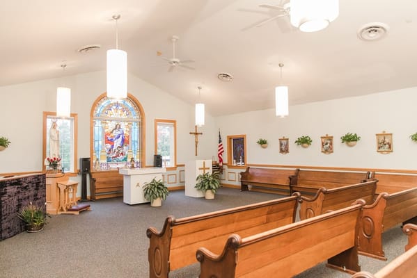Interior view of a chapel with pews and stained glass window