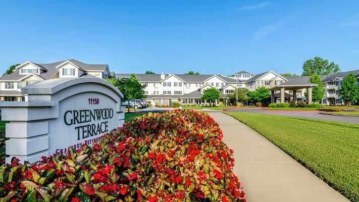 Entrance sign of Holiday Greenwood Terrace surrounded by flowers.
