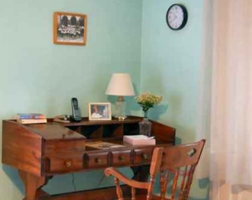 Wooden desk and chair with a lamp, phone, and flower vase against a teal wall.