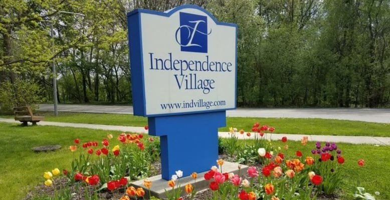 Sign for Independence Village surrounded by colorful flowers