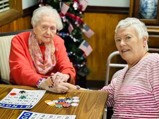 Two senior women engaged in a bingo game at a table