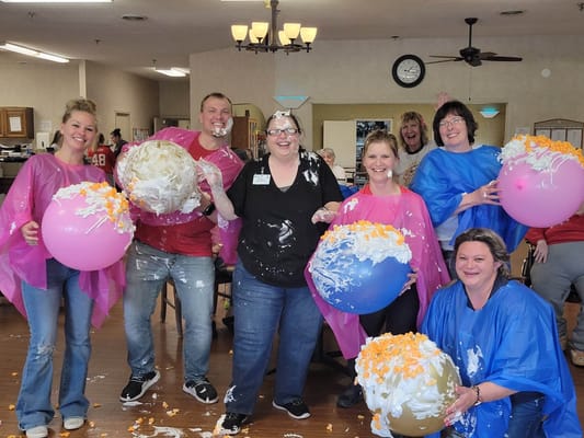 Group of staff and residents participating in a pie fight with colorful balloons and whipped cream.