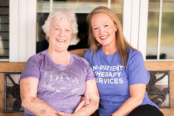 A resident and staff member smiling together on a bench