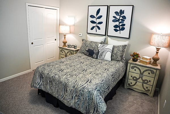 A well-decorated bedroom featuring a queen-sized bed, two bedside tables with lamps, and decorative wall art.