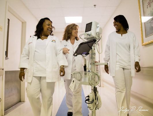 Three staff members in white coats walking down a nursing facility hallway