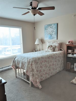 A cozy bedroom with a single bed, floral bedding, and natural light from a window.