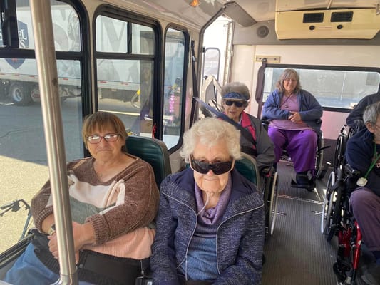 Senior residents seated on a bus, smiling and wearing sunglasses.