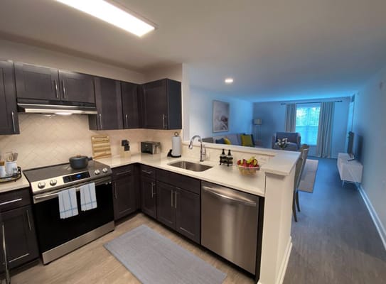 View of a modern kitchen with stainless steel appliances and a living room in the background