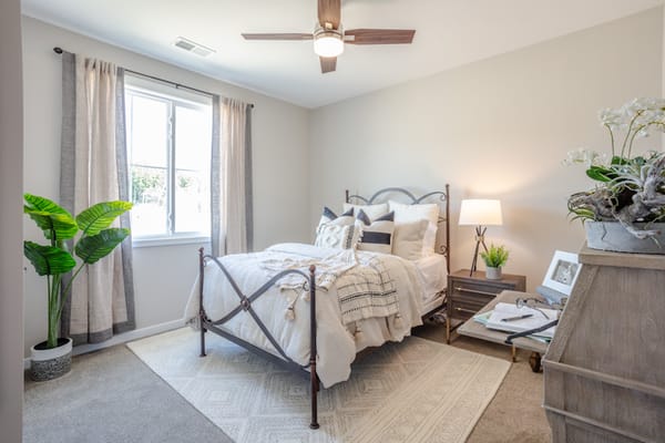 A cozy bedroom with a bed, nightstand, and a plant near the window.