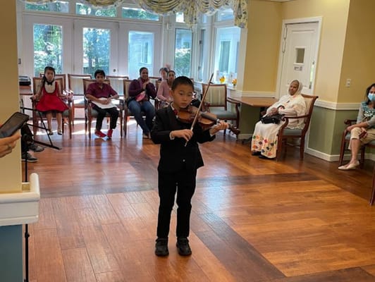 A young boy in a black suit playing the violin in front of an audience.