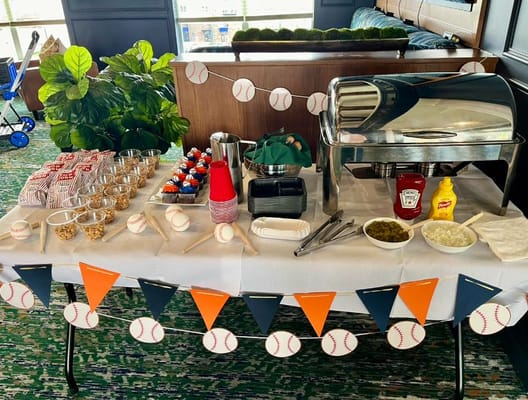 A table set with baseball-themed snacks, including cupcakes, popcorn, and condiments.