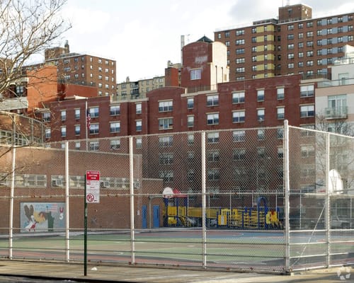 View of a playground and basketball court behind a fence.