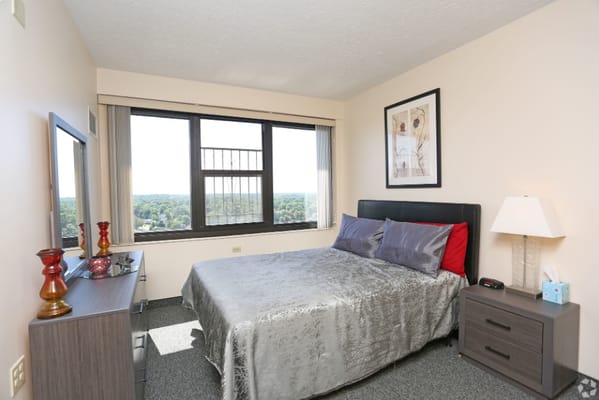 A well-furnished bedroom featuring a bed, dresser, and large windows with a view.