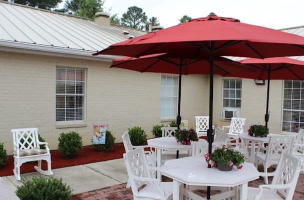 Outdoor patio with red umbrellas and white tables surrounded by greenery