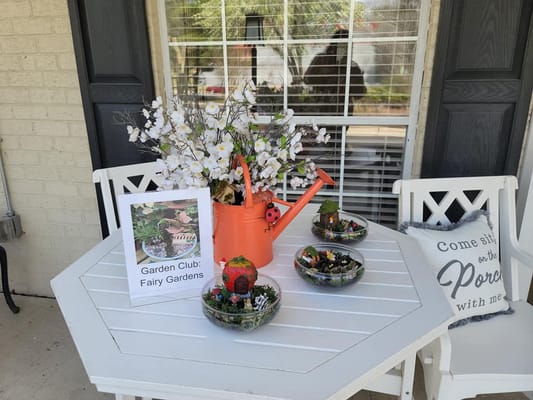Table display with fairy gardens, watering can, and floral arrangement.