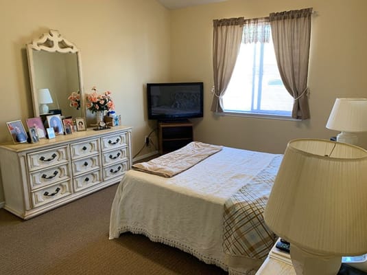 A bedroom with a bed, dresser, TV, and window