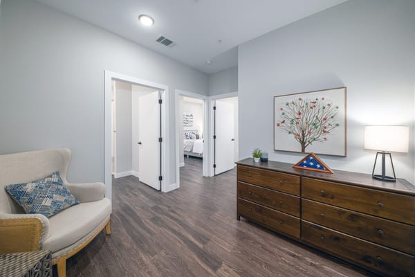 Interior view of a hallway with a chair, dresser, and artwork.