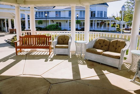 Outdoor seating area with a wooden bench and white wicker chairs
