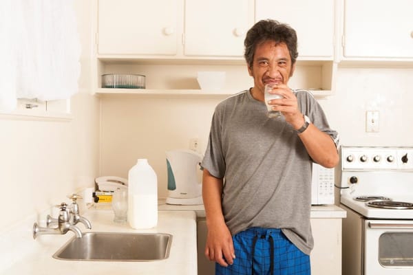 Man holding a glass of milk in a kitchen setting
