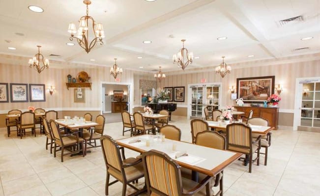Bright dining area with tables and chairs in a memory care facility.
