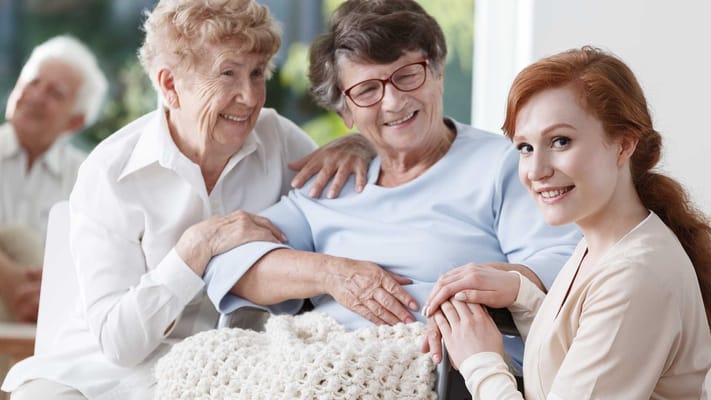 Two senior women smiling and bonding with a caregiver