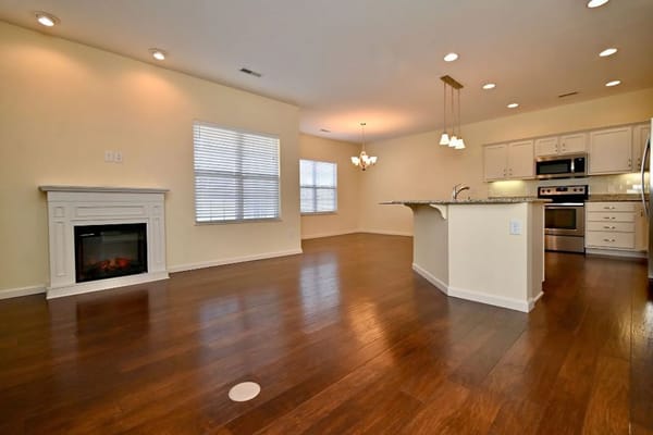 Spacious living room with a kitchen area, featuring hardwood floors and large windows.