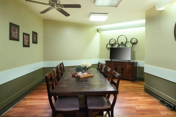 A dining room with a large wooden table and chairs, decorated with flowers.