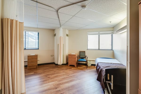 A spacious residential room with hardwood flooring, a bed, and wooden furniture.