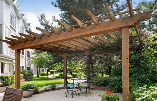Wooden pergola over a patio with chairs and greenery