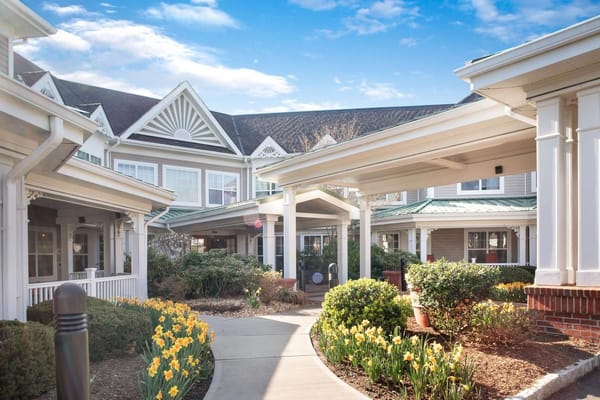 Pathway with blooming flowers leading to the entrance of Sunrise of Woodcliff Lake.