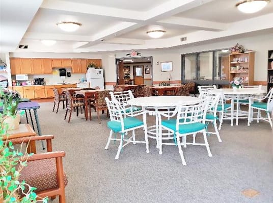A spacious common area with tables and chairs in a senior living facility.