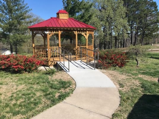 Wooden gazebo with a red roof surrounded by flowers and trees