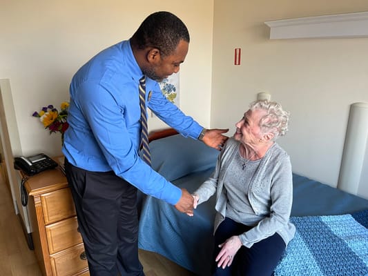 A staff member shakes hands with a senior resident in a cozy room.