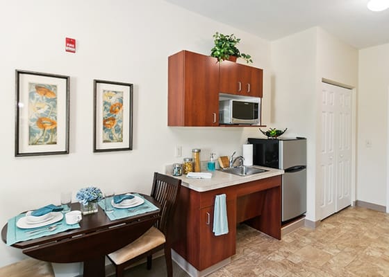 A kitchenette with a dining table set for two, featuring modern appliances and decor.