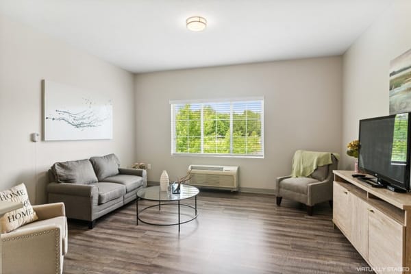 A furnished living room with a couch, armchair, and large window