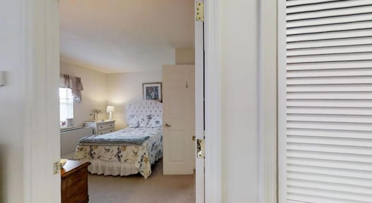 A view of a cozy bedroom featuring a floral bedspread, bedside lamp, and window.