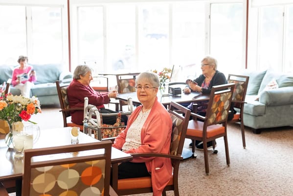 Seniors socializing in a comfortable lounge area with flowers on the table.