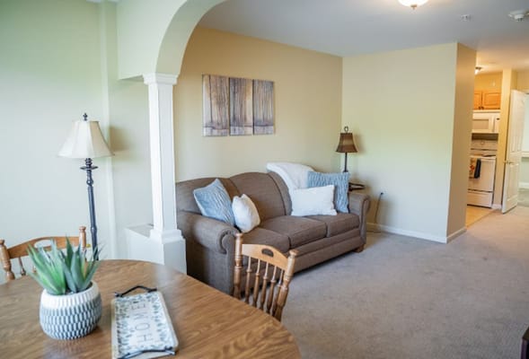 A cozy living room with a sofa, dining table, and kitchen in the background.