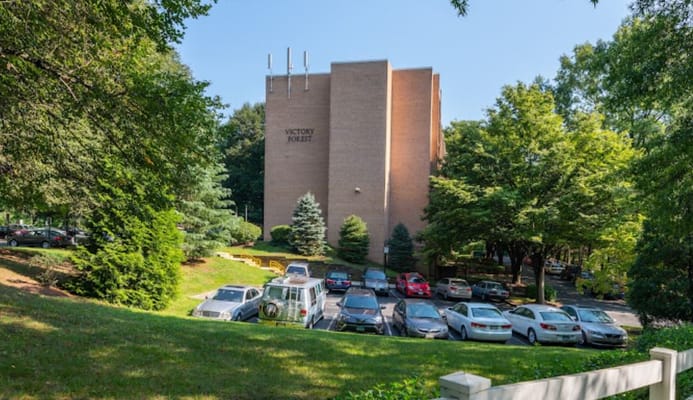 Exterior view of Victory Forest senior living facility with greenery and parking lot.